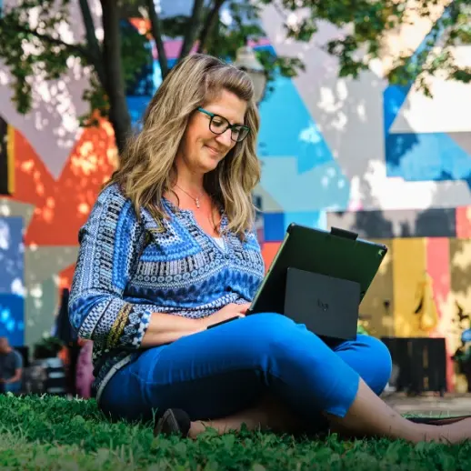 Woman sitting in grass working on laptop
