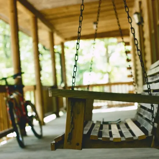 a wooden swinging bench on a deck, with a bike next to it
