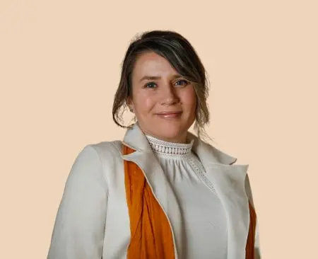 woman smiling wearing white jacket over white top with orange scarf